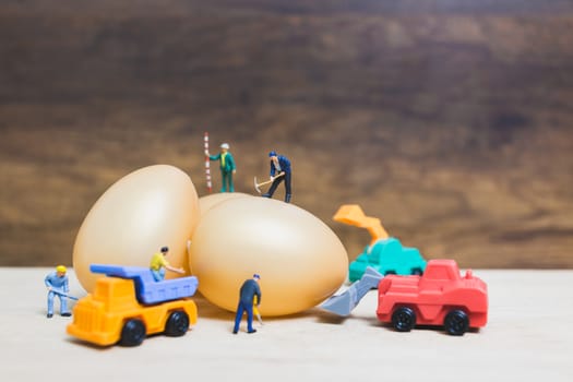 Miniature people work at Easter-eggs for Easter day on wooden background