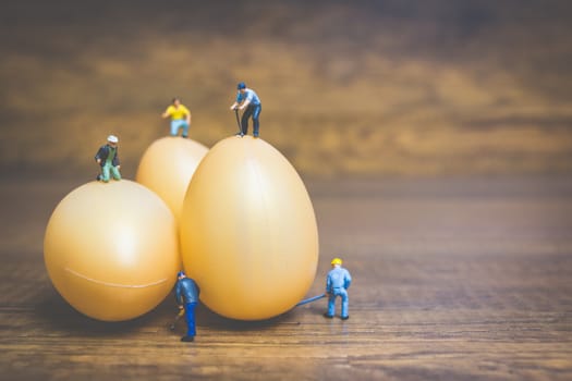 Miniature people work at Easter-eggs for Easter day on wooden background