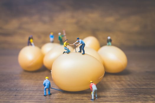 Miniature people work at Easter-eggs for Easter day on wooden background