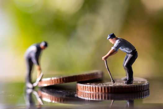 Miniature people worker holding tool on coins with green bokeh background , Construction concept
