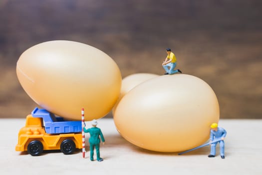 Miniature people work at Easter-eggs for Easter day on wooden background