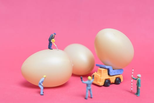 Miniature people work at Easter-eggs for Easter day on pink background
