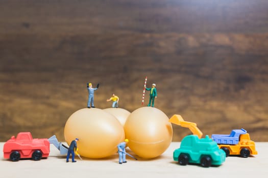 Miniature people work at Easter-eggs for Easter day on wooden background