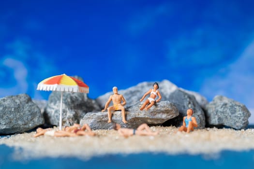 Miniature people wearing swimsuit relaxing on the beach with blue background , Summer time concept