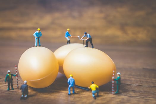 Miniature people work at Easter-eggs for Easter day on wooden background