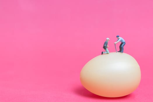 Miniature people work at Easter-eggs for Easter day on pink background