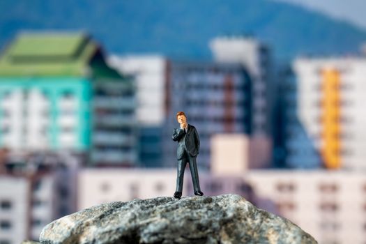 Miniature people , Businessman standing on The rock with building background