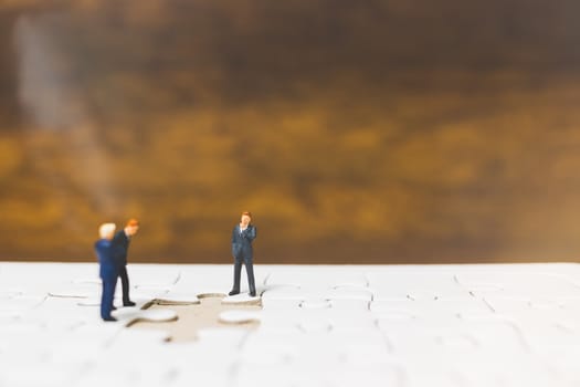 Miniature people: Businessman standing on jigsaw with wooden background : Business concept.