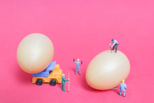Miniature people work at Easter-eggs for Easter day on pink background