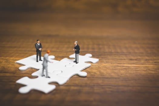 Miniature people: Businessman standing on jigsaw with wooden background : Business concept.
