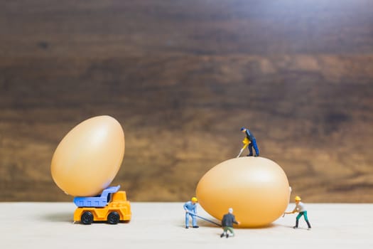 Miniature people work at Easter-eggs for Easter day on wooden background