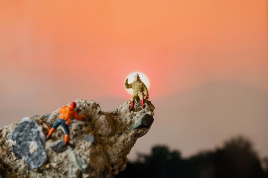 Miniature people: Hikers climbing up on the rock . Sport and leisure concept.