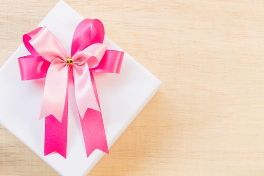 Pink ribbon bow and white gift box on wooden background
