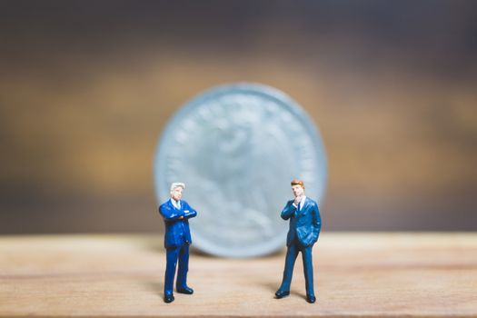 Miniature people : Businessman standing near coin with wooden background : Business concept.