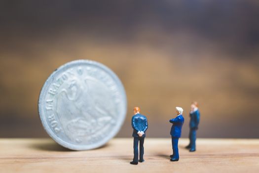 Miniature people : Businessman standing near coin with wooden background : Business concept.