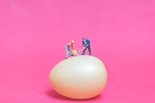 Miniature people work at Easter-eggs for Easter day on pink background