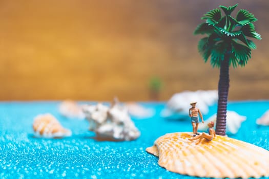 Miniature people wearing swimsuit relaxing on a seashell with blue glitter background