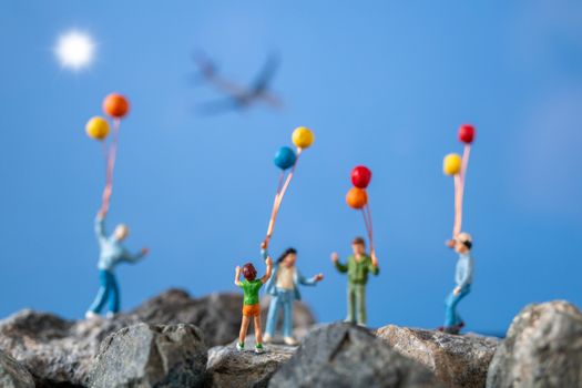 Miniature people , Happy family holding balloon on The rock with blue sky background