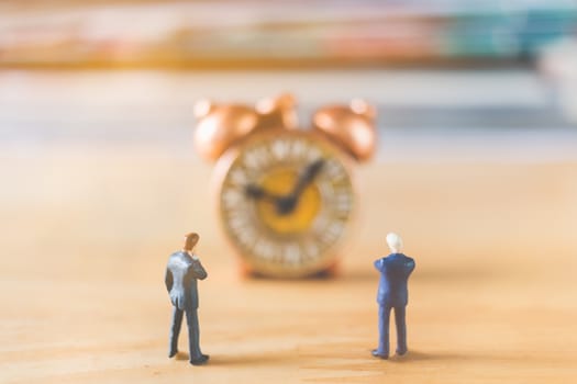 Miniature people: Businessman standing with Ancient clock on wooden background