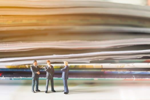 Miniature people: Businessman standing and stack of book with warm lighting background