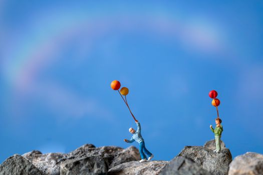 Miniature people , Happy family holding balloon on The rock with blue sky background