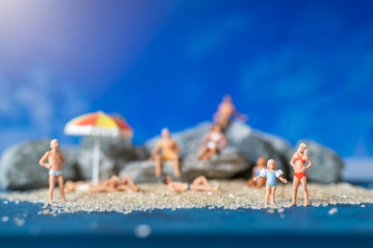 Miniature people wearing swimsuit relaxing on the beach with blue background , Summer time concept