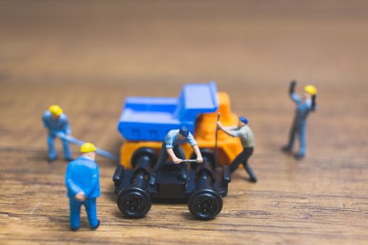 Miniature people : Worker repairing wheel of a truck on wooden background