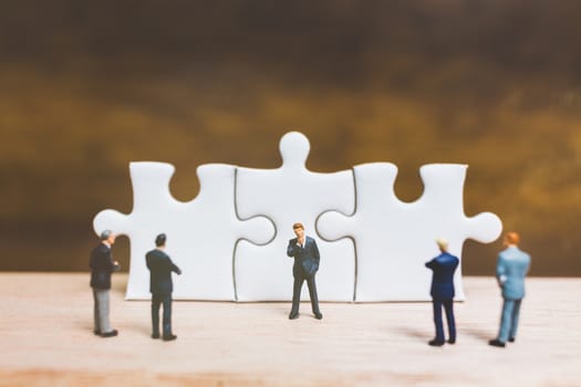 Miniature people: Businessman standing on jigsaw with wooden background : Business concept.