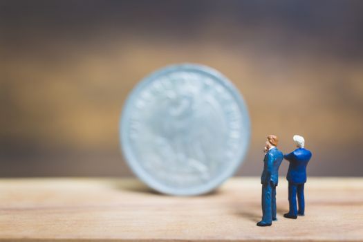 Miniature people : Businessman standing near coin with wooden background : Business concept.