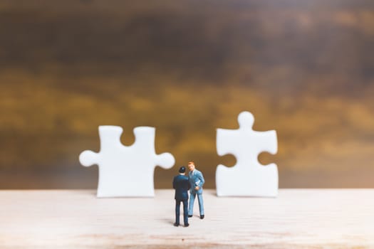 Miniature people: Businessman standing on jigsaw with wooden background : Business concept.