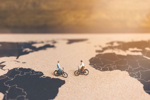 Miniature people travelers riding bicycle on world map , Traveling and exploring the world Concept