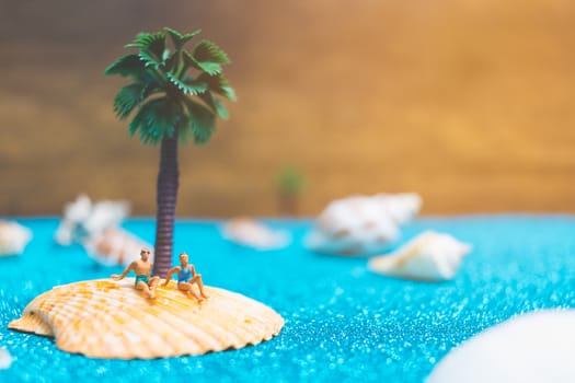 Miniature people wearing swimsuit relaxing on a seashell with blue glitter background