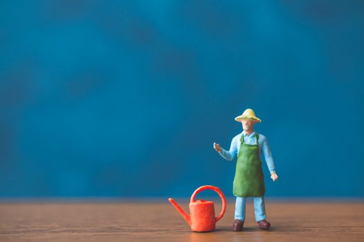 Miniature people gardener standing in front of a blue wall background