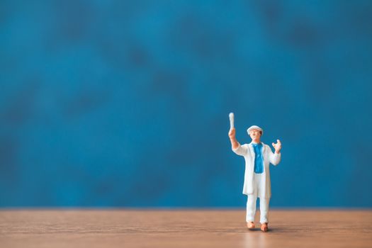 Miniature people holding brush in front of a blue wall background