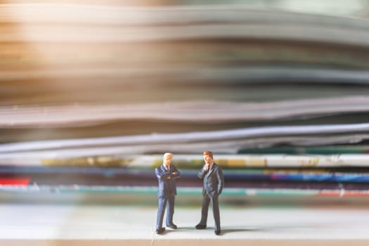 Miniature people: Businessman standing and stack of book with warm lighting background