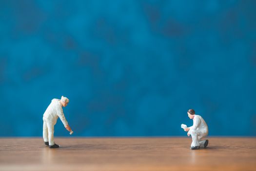 Miniature people holding brush in front of a blue wall background