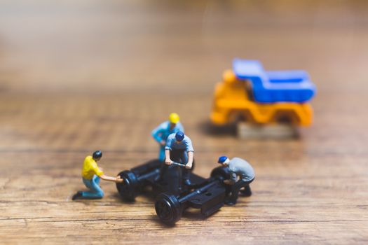 Miniature people : Worker repairing wheel of a truck on wooden background