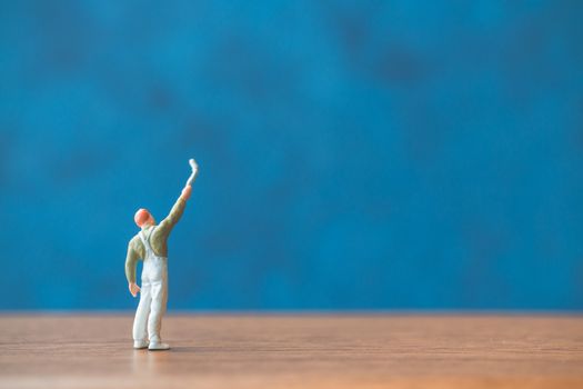 Miniature people holding brush in front of a blue wall background