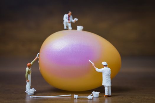 Miniature people :Painter is painting Easter-eggs for Easter day on wooden background