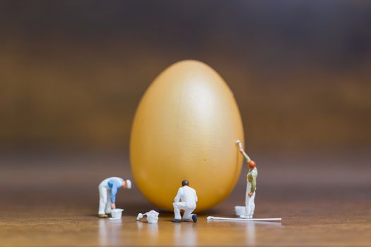 Miniature people :Painter is painting Easter-eggs for Easter day on wooden background