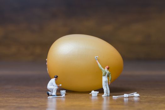 Miniature people :Painter is painting Easter-eggs for Easter day on wooden background