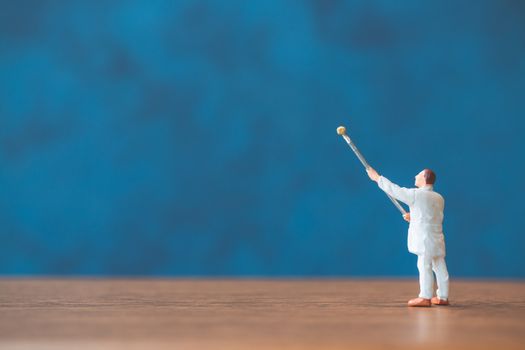 Miniature people holding brush in front of a blue wall background