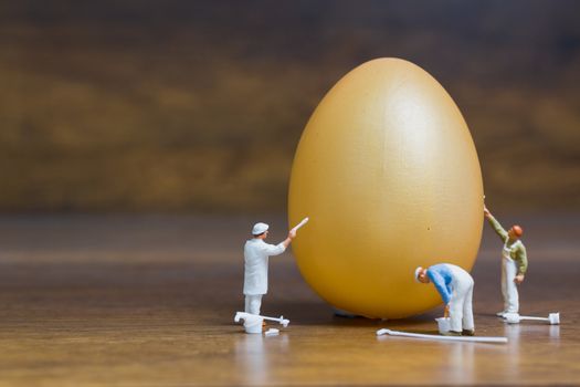 Miniature people :Painter is painting Easter-eggs for Easter day on wooden background