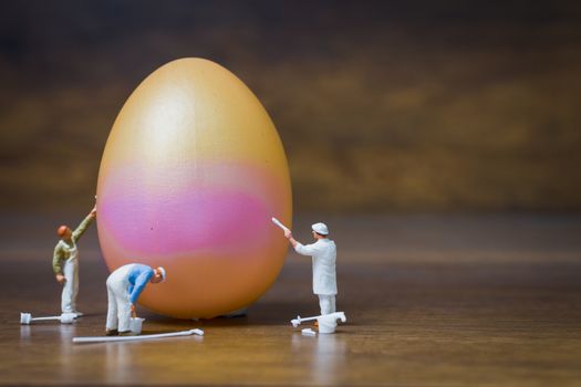 Miniature people :Painter is painting Easter-eggs for Easter day on wooden background