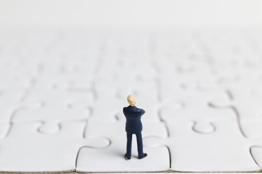 Miniature people: Businessman standing on white jigsaw. Business concept.