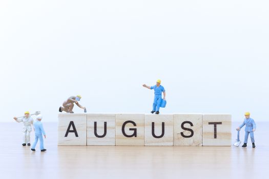 August words with Miniature people worker on wooden floor
