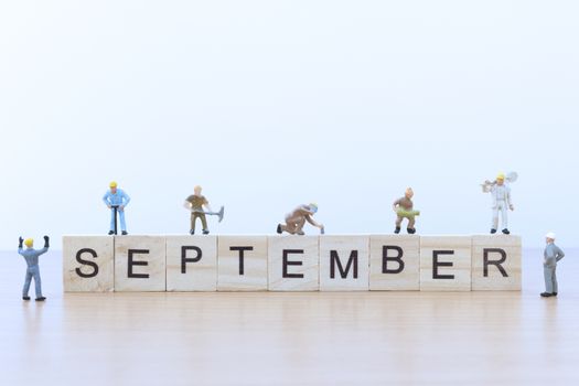 September words with Miniature people worker on wooden floor
