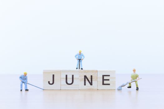June words with Miniature people worker on wooden floor
