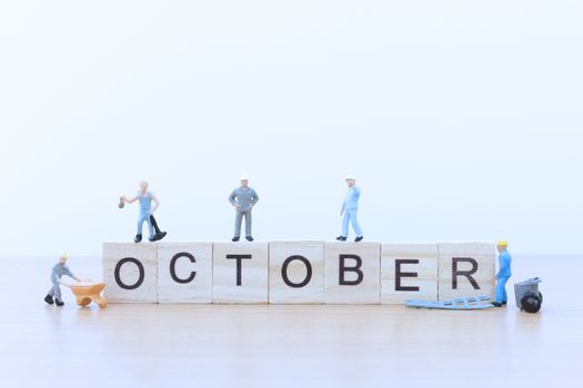 October words with Miniature people worker on wooden floor
