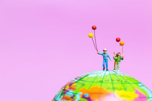 Miniature people : Happy family holding balloon on The globe with pink background and copy space for text